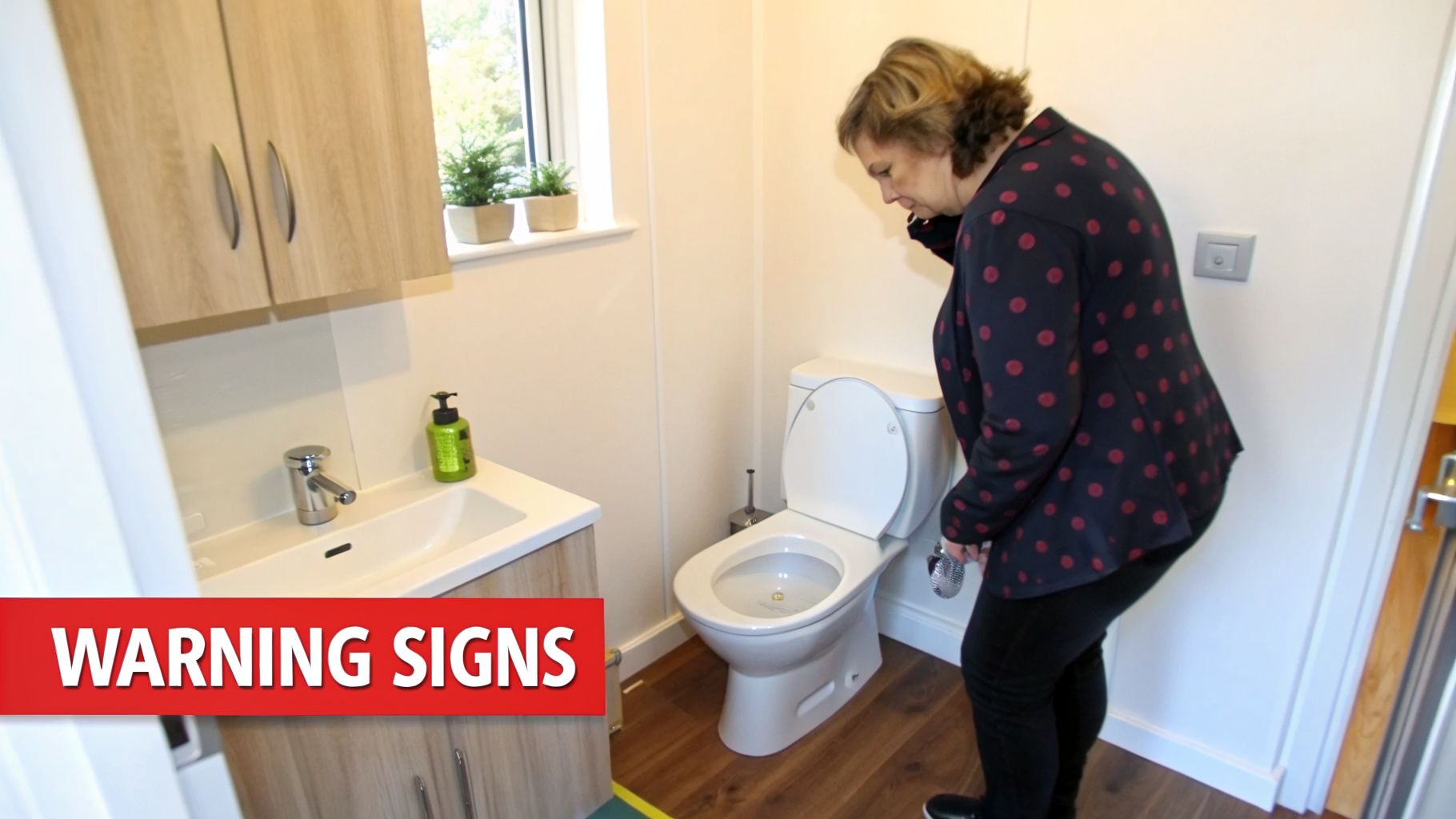 A woman inspects a toilet in a bathroom, suggesting a plumbing issue.